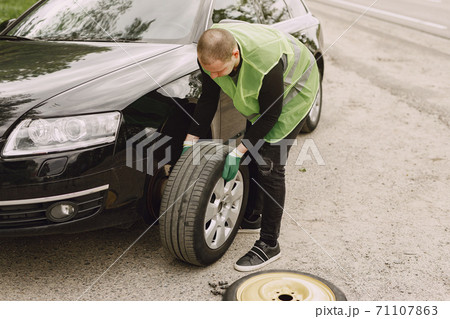 Man changing broken wheel on car 71107863