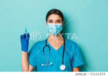 Concept of covid-19 and quarantine concept. Close-up of beautiful female doctor in medical mask, rubber gloves and scrubs, ready to vaccinate patient, holding syringe with coronavirus vaccine 71111374