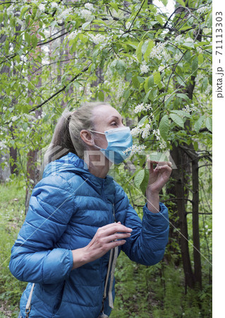 A woman in a park sniffs a bird cherry in a protective mask on her face 71113303
