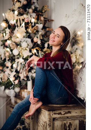 Woman with a Christmas Gift sitting on acncient commode decorated for xmas. Fir tree at background 71113470