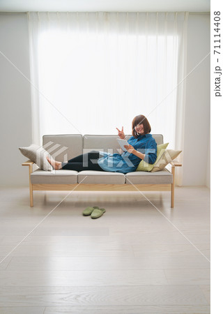 お家時間をソファでくつろぎながらタブレットを使って過ごす若い女性 71114408