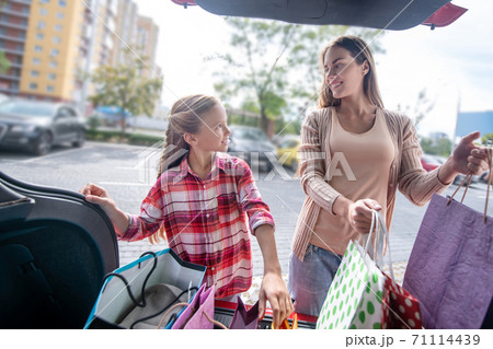Fair-haired girl and young woman looking at each other, taking out shopping bags from car boot Fair-haired girl and young woman looking at each other, taking out shopping bags from car boot 71114439