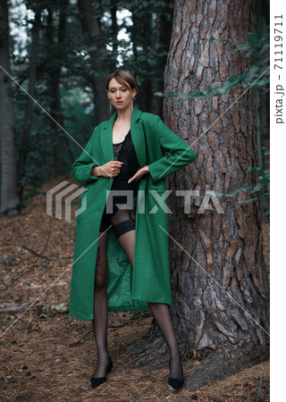 Fashionable young woman in green coat posing in a forest near the tree Fashionable young woman in green coat posing in a forest near the tree 71119711