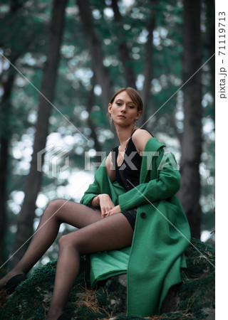 Fashionable young woman in green coat posing in a forest Fashionable young woman in green coat posing in a forest 71119713