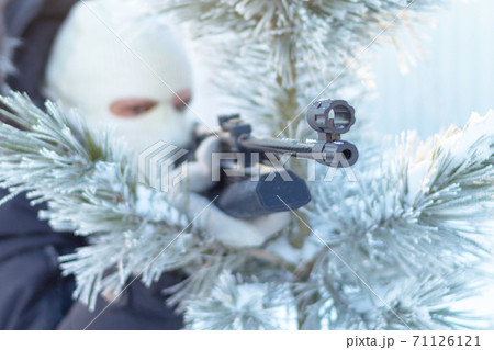 Masked man aims with rifle in winter forest. 71126121