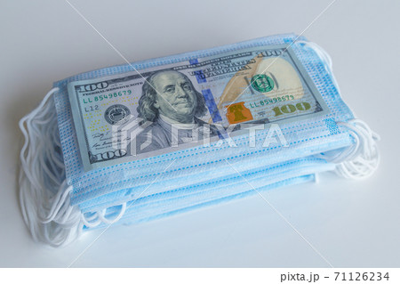 A pack of medical masks and a 100 dollars bills as a symbol of higher prices and a deficiency in the protection of the respiratory tract from viruses. 71126234