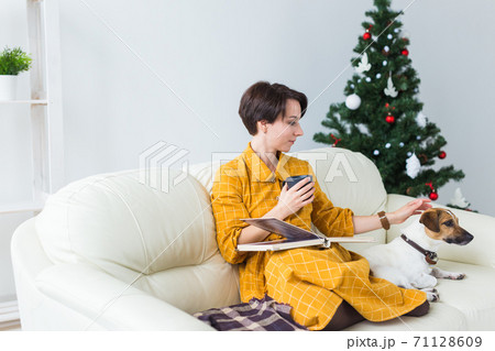 Woman reads book in front of Christmas tree with dog jack russell terrier. Christmas, holidays and pet. 71128609