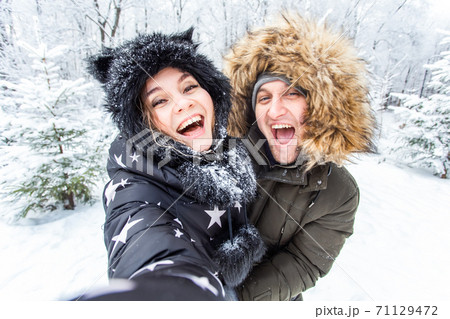 Technologies and relationship concept - Happy smiling couple taking a selfie in a winter forest outside 71129472