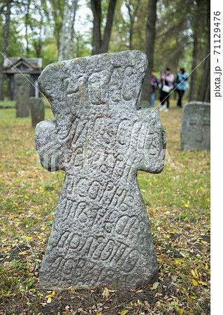 A worn sandstone grave marker in the shade on a very bright day. There is no text visible on the stone, but there is some moss on the top. Tombstone and graves in an ancient church graveyard. toned 71129476