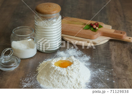 Kneading the Dough. There is flour on the table with an egg in the middle. In glass jars for storing flour, salt. Nearby are wooden planks 71129838