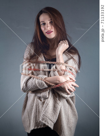 Portrait of young binded woman with rope on sweater on grey background 71133192