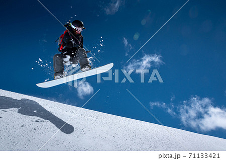 Young woman on a snowboard makes a flight after jumping from a snowy ledge against a dark blue sky high in the mountains in winter Young woman on a snowboard makes a flight after jumping from a snowy ledge against a dark blue sky high in the mountains in winter 71133421