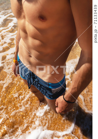 sexy naked tanned torso muscle press press unknown man on golden beach stands in water with waves and foam sexy naked tanned torso muscle press press unknown man on golden beach stands in water with waves and foam 71133439