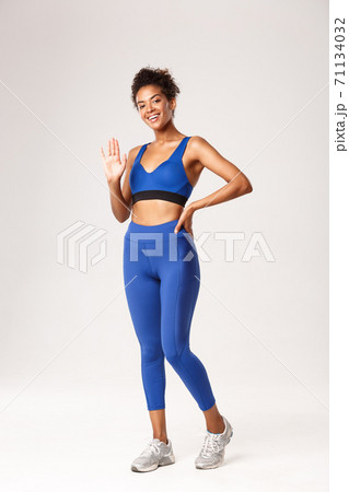 Full length of smiling girl in gym clothing saying hello, standing over white background in sportswear and waving hand, greeting someone, standing over white background Full length of smiling girl in gym clothing saying hello, standing over white background in sportswear and waving hand, greeting someone, standing over white background 71134032