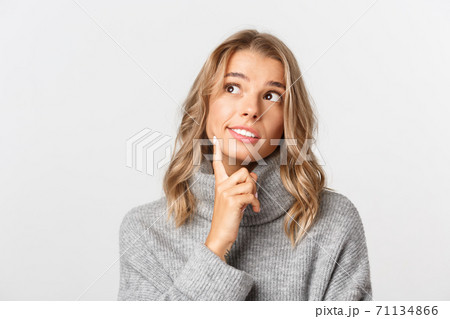 Close-up of dreamy cute girl with blond hair, wearing grey sweater, looking at upper left corner and thinking, daydreaming of something, white background Close-up of dreamy cute girl with blond hair, wearing grey sweater, looking at upper left corner and thinking, daydreaming of something, white background 71134866