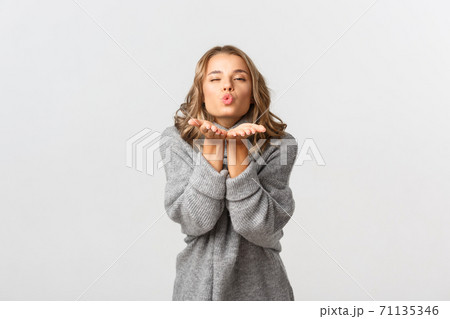 Portrait of attractive lovely woman in grey sweater sending air kiss, standing over white background Portrait of attractive lovely woman in grey sweater sending air kiss, standing over white background 71135346
