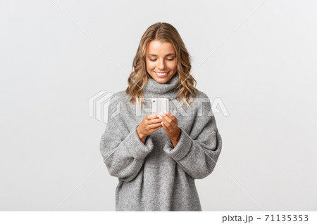 Portrait of young caucasian girl with short blond hair using mobile phone, messaging online, standing over white background Portrait of young caucasian girl with short blond hair using mobile phone, messaging online, standing over white background 71135353