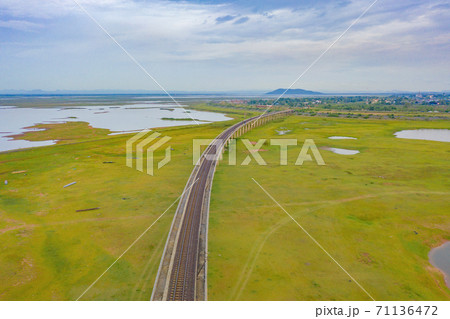 Aerial view of Thai local train on railway bridge at Pa Sak Jolasid Dam, the biggest reservoir in central Thailand, in Lopburi province with cloudy sky in transportation and travel concept. 71136472