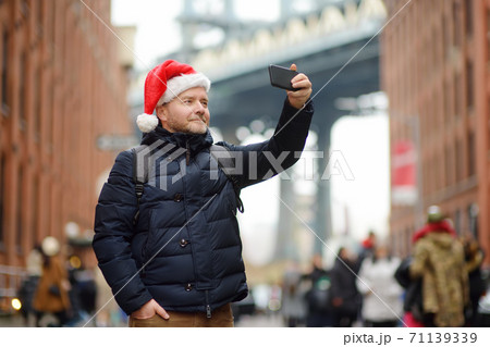Middle aged man tourist in Santa Claus hat takes selfie on streete in New York City on Christmas Eve Middle aged man tourist in Santa Claus hat takes selfie on streete in New York City on Christmas Eve 71139339