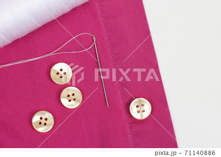Coil with white threads and a needle and sewn pearl buttons on the shirt 71140886