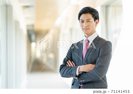 オフィスの廊下に腕組みをして立つ若い笑顔の男性 71141453