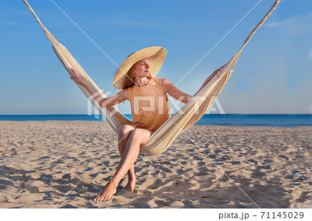 journey to the sea. a girl in a yellow dress and hat is sitting in a hammock on the beach. travel during the holiday season. copy space journey to the sea. a girl in a yellow dress and hat is sitting in a hammock on the beach. travel during the holiday season. copy space 71145029