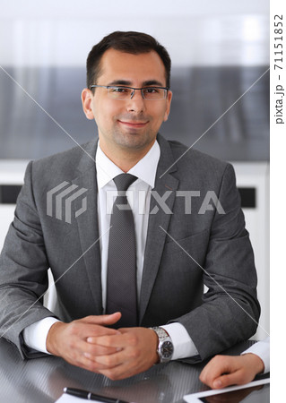 Businessman headshot at meeting in modern office. Entrepreneur sitting at the table with colleagues. Teamwork and partnership concept. Grey blazer suits to happy smiling manager 71151852