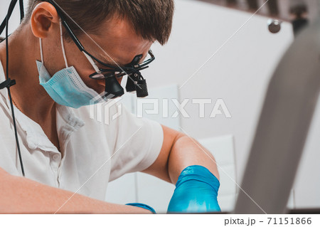 Dentist in binoculars, use of binoculars in dental treatment, dentist in the office, magnifying glass for binoculars. 71151866