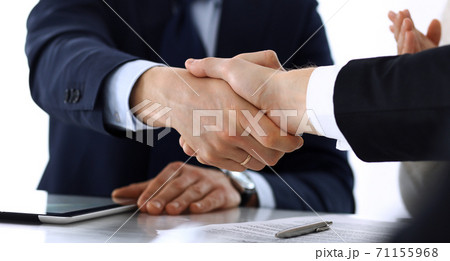 Business people shaking hands after contract signing at the glass desk in modern office. Unknown businessman with colleagues at meeting or negotiation. Teamwork, partnership and handshake concept 71155968