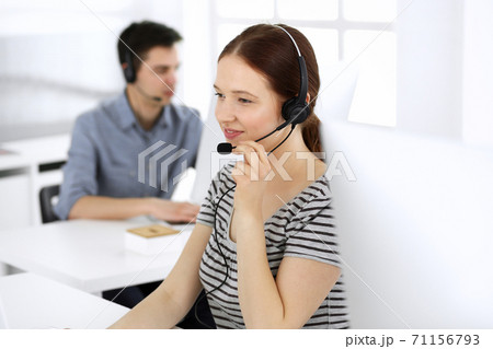 Group of operators at work. Call center. Focus on beautiful woman receptionist in headset at customer service. Business concept and casual striped clothing style Group of operators at work. Call center. Focus on beautiful woman receptionist in headset at customer service. Business concept and casual striped clothing style 71156793