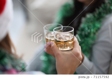 They are holding two glasses with liquid in their hands against background of New Year's garlands. They are holding two glasses with liquid in their hands against background of New Year's garlands. 71157592