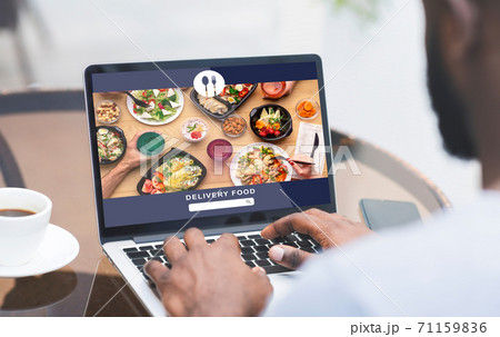 Modern food and fast delivery at home or office. African american man uses laptop and order meal Modern food and fast delivery at home or office. African american man uses laptop and order meal 71159836