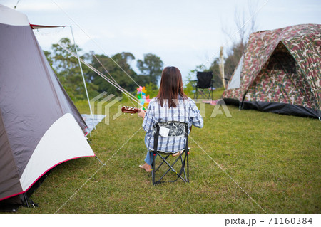 Asian woman sitting on picnic chair and playing guitar while camping with family in the camping site in the beautiful nature. Family enjoy with nature and camping concept. Asian woman sitting on picnic chair and playing guitar while camping with family in the camping site in the beautiful nature. Family enjoy with nature and camping concept. 71160384