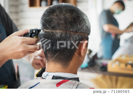 Asian young man who have gray hair being haircut with electric clipper machine by professional barber in barbershop. 71160565