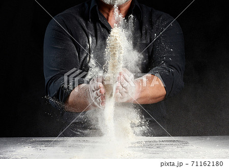 chef in black uniform sprinkles white wheat flour in different directions, product scatters dust chef in black uniform sprinkles white wheat flour in different directions, product scatters dust 71162180