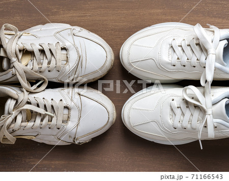 Pair of old dirty white sneakers in front of new clean one on a brown background. 71166543