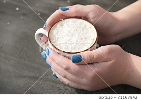womans hands with blue manicure holding a cup of hot coffee 71167842