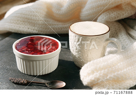 white cup of coffee and raspberry jelly near white knitted fabric. 71167888