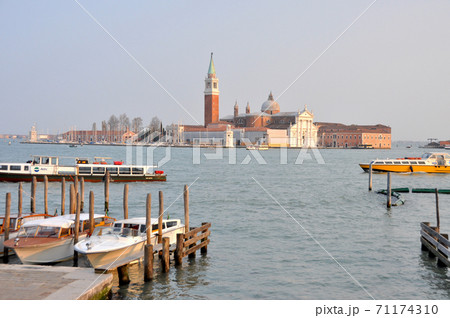 ヴェニス 係留されたゴンドラと夕陽に映えるサン ジョルジョ マジョーレ島の教会の写真素材