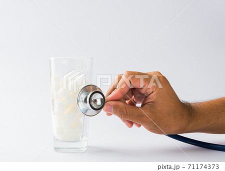 Hand of doctor hold stethoscope check on glass full of white sugar cube Hand of doctor hold stethoscope check on glass full of white sugar cube 71174373