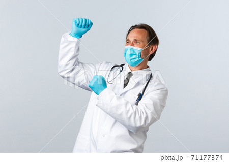 Covid-19, preventing virus, healthcare workers and vaccination concept. Happy triumphing doctor in medical mask and gloves celebrating good news, fist pump and dancing, white background Covid-19, preventing virus, healthcare workers and vaccination concept. Happy triumphing doctor in medical mask and gloves celebrating good news, fist pump and dancing, white background 71177374