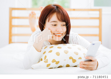 ベッドで寝転がってスマホを使う女性 ベッドで寝転がってスマホを使う女性 71180451