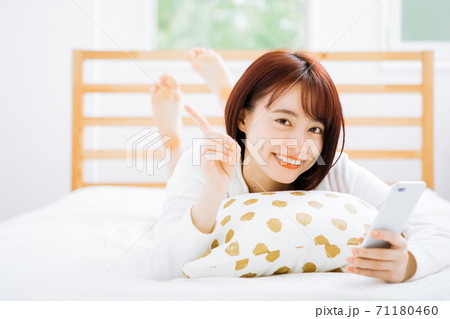 ベッドで寝転がってスマホを使う女性 ベッドで寝転がってスマホを使う女性 71180460
