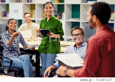 Positive team. Group of young happy multi racial business people communicating and sharing ideas while working together in the modern office Positive team. Group of young happy multi racial business people communicating and sharing ideas while working together in the modern office 71187127