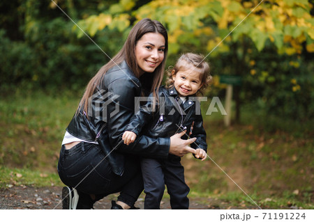 Little girl walking with her mom in forest. Mother with her daughter in leather jackets 71191224