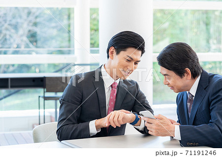 スマートウォッチを見る若い男性とスマホを見るシニアの男性 71191246