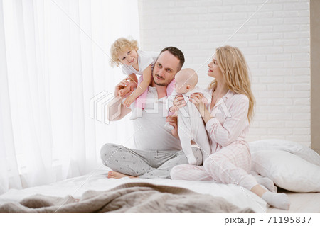 A young Caucasian family with two children daughters in a white home interior. Home clothes. A young Caucasian family with two children daughters in a white home interior. Home clothes. 71195837