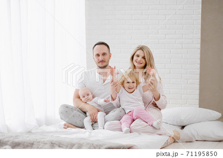 A young Caucasian family with two children daughters in a white home interior. Home clothes. A young Caucasian family with two children daughters in a white home interior. Home clothes. 71195850