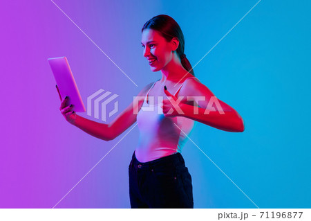 Young caucasian woman's portrait on gradient blue-purple studio background in neon light 71196877