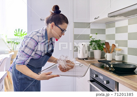 Woman preparing pork in baking sleeve at home, puts tray of meat in oven Woman preparing pork in baking sleeve at home, puts tray of meat in oven 71201385